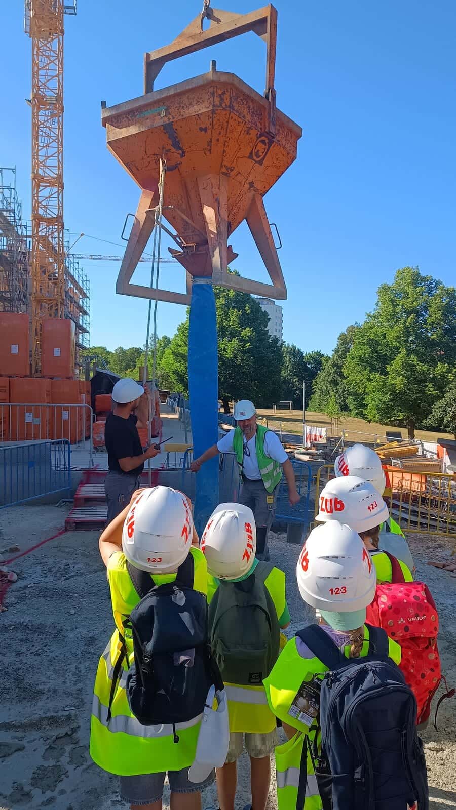 Betreten der Baustelle erlaubt 2026 - Zweitklässler mit Bauhelmen und Warnwesten besichtigen die Baustelle mit Kran und Betonkübel