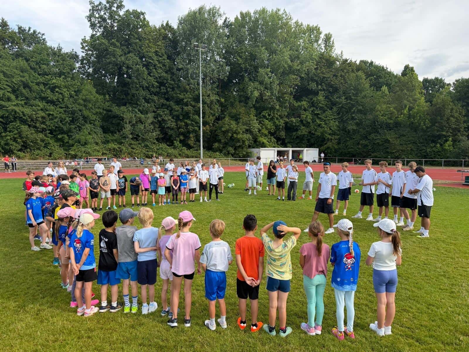 Bundesjugendspiele 2026 - Großer Kreis aus Kindern und Sportmentoren zum Aufwärmen auf dem Rasen