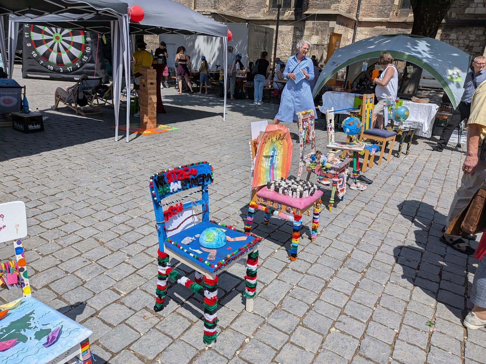 Wir sitzen alle an einem Tisch 2026 - Bunt gestaltete Schülerstühle auf dem Münsterplatz, im Vordergrund ein Stuhl mit aufgemaltem Globus
