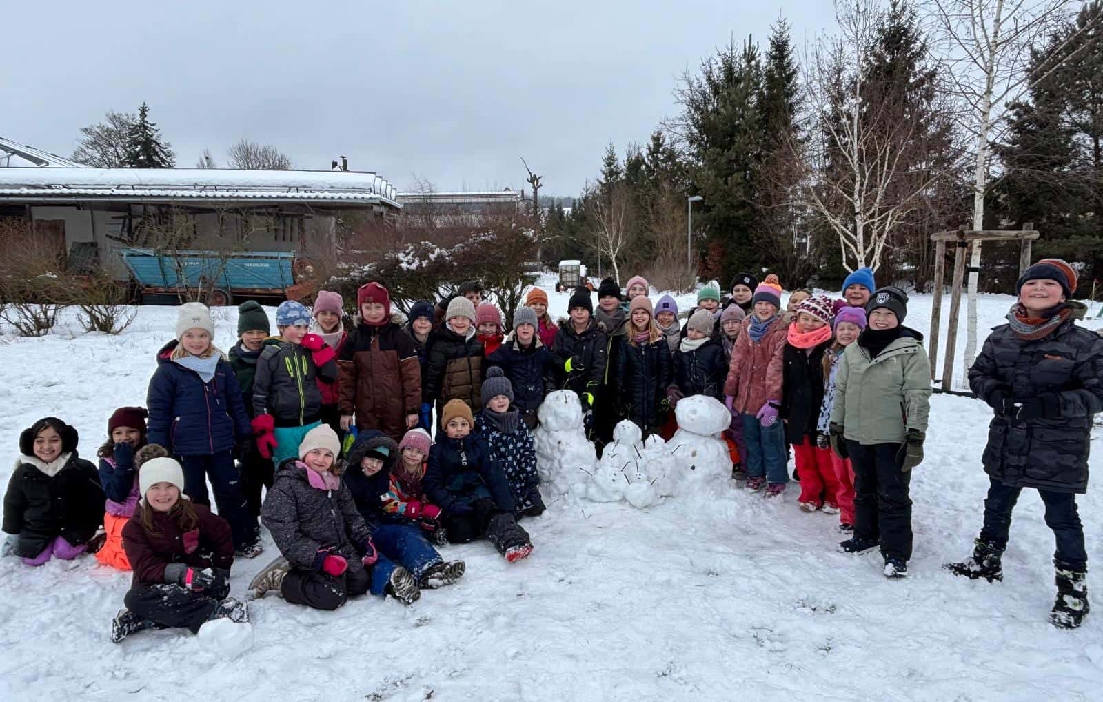 Schneetag 2026 - Gruppenfoto der Klassen 1 und 2 mit Schneemann im Schnee