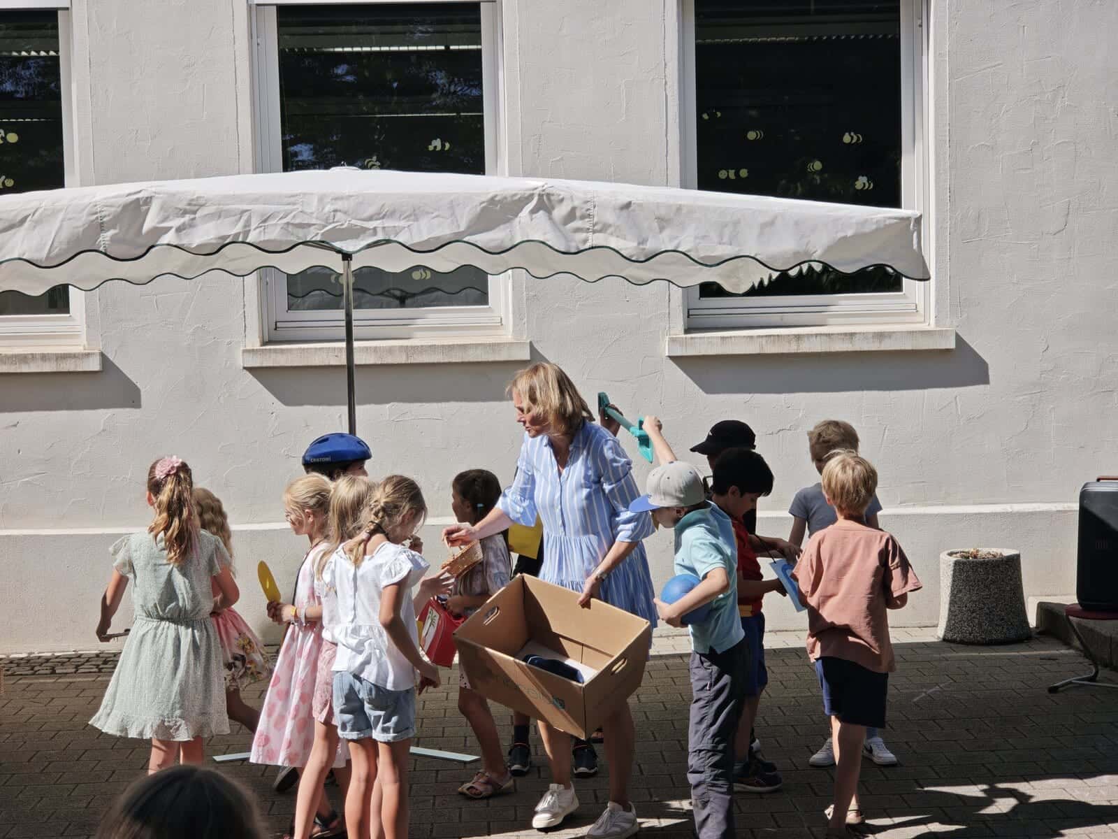 Schulfest 2026 - Eine Lehrerin verteilt aus einem Karton Wassereis an die wartenden Kinder