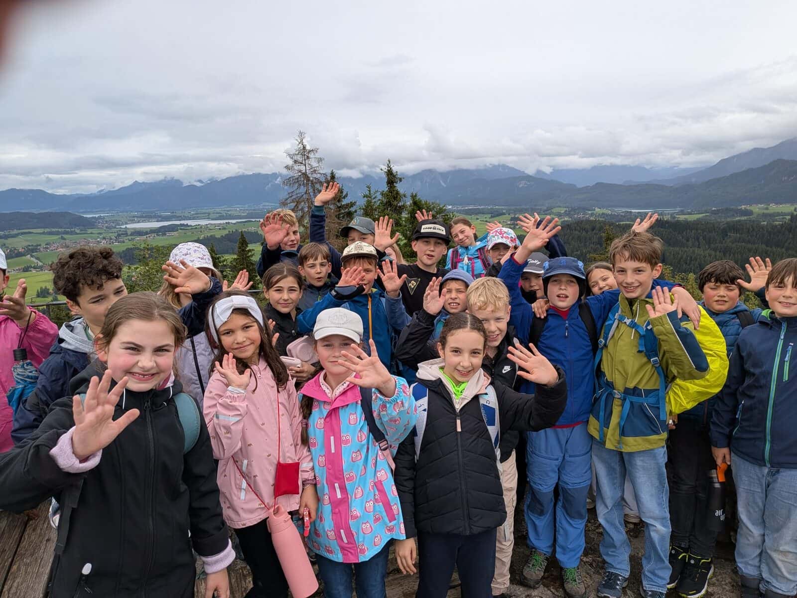 Schullandheim 2026 - Klasse 3/4 winkt auf einem Aussichtspunkt mit Alpenpanorama