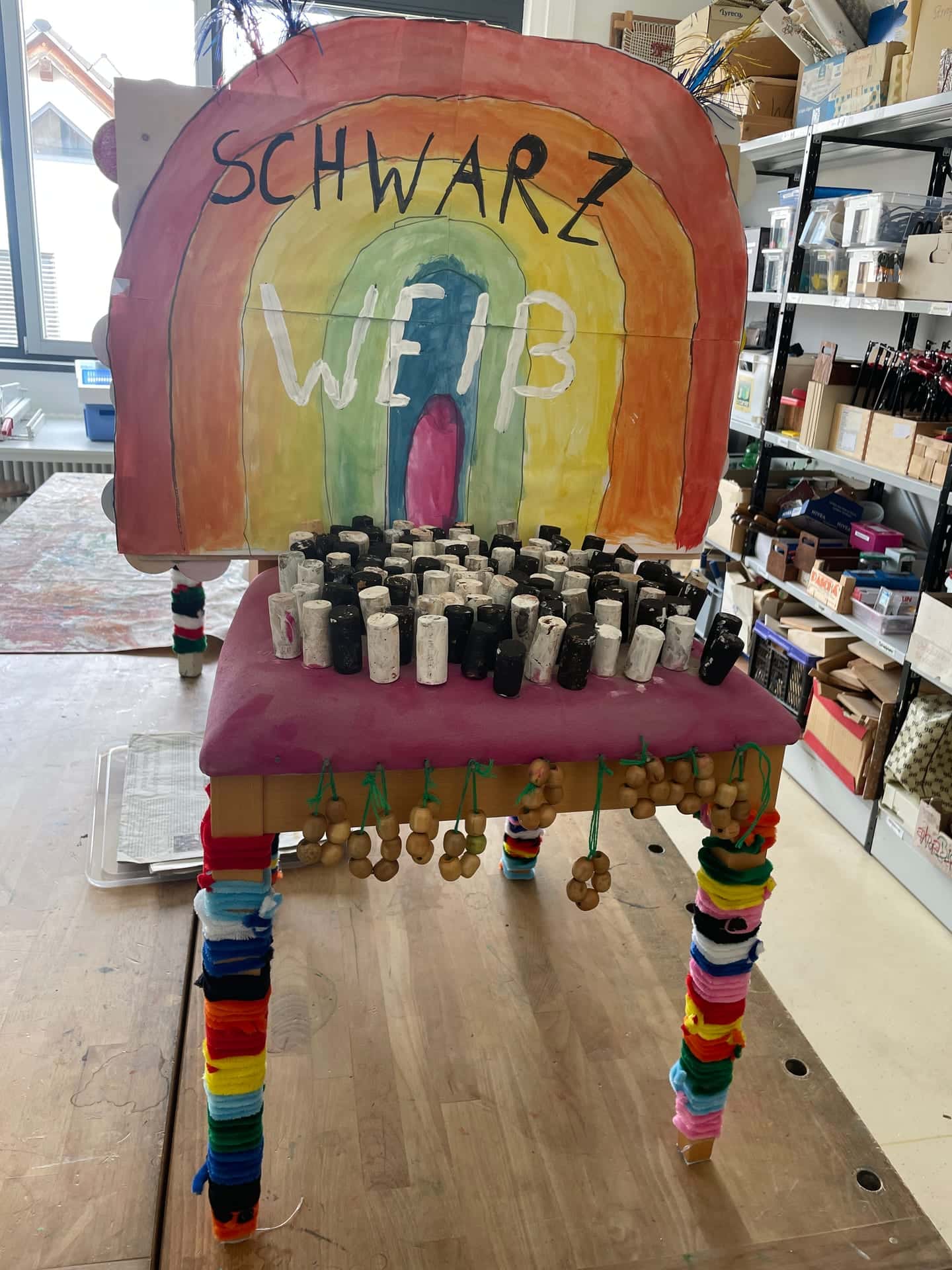 Stuhl-Projekt 2026 - Stuhl mit Regenbogen-Lehne Schwarz Weiß und bunten Figurengruppen