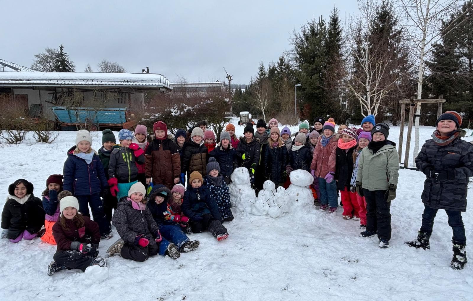 Schneetag 2026 - Gruppenfoto der Klassen 1 und 2 mit Schneemann im Schnee